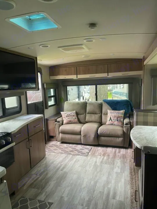 This spacious RV rental interior features a sofa, kitchen counter, overhead cabinets, and TV, all in light, neutral tones.. Grand Design Imagine 2022