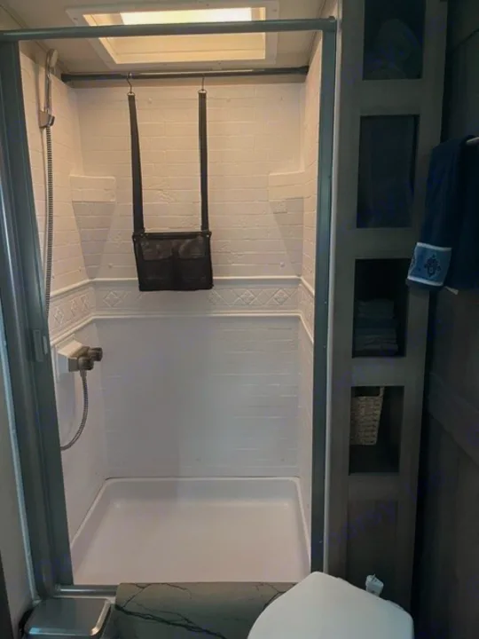 RV rental bathroom: compact shower with overhead skylight, shelving unit, and toilet visible.. Grand Design Imagine 2022