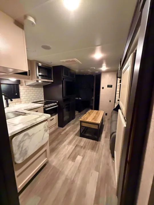 Modern rv rental interior: well-lit kitchen with subway tile, living area, and light wood-look flooring.. Jayco Jay Feather 2023