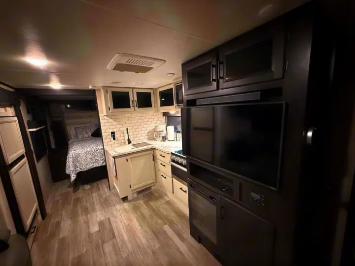 Modern rv rental interior featuring a bright kitchen with subway tiles, TV area, and a cozy bedroom. Ready for adventure.. Jayco Jay Feather 2023