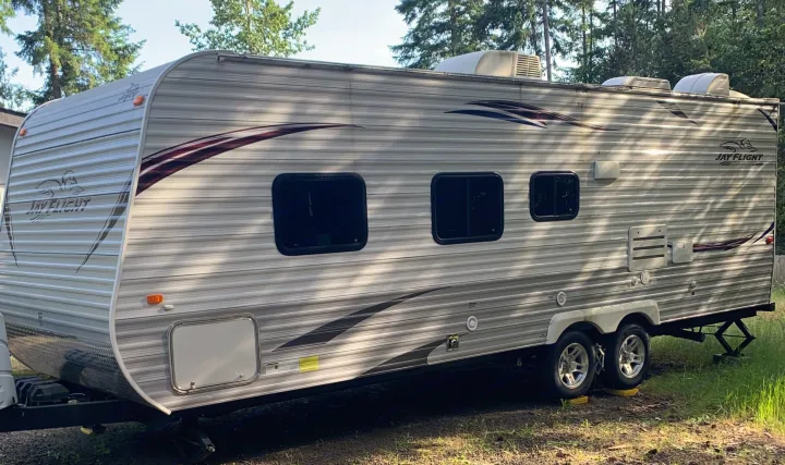 A grey and white Jayco Jay Flight travel trailer RV rental, parked in a wooded area, ready for your next adventure.. Jayco Jay Flight 2013