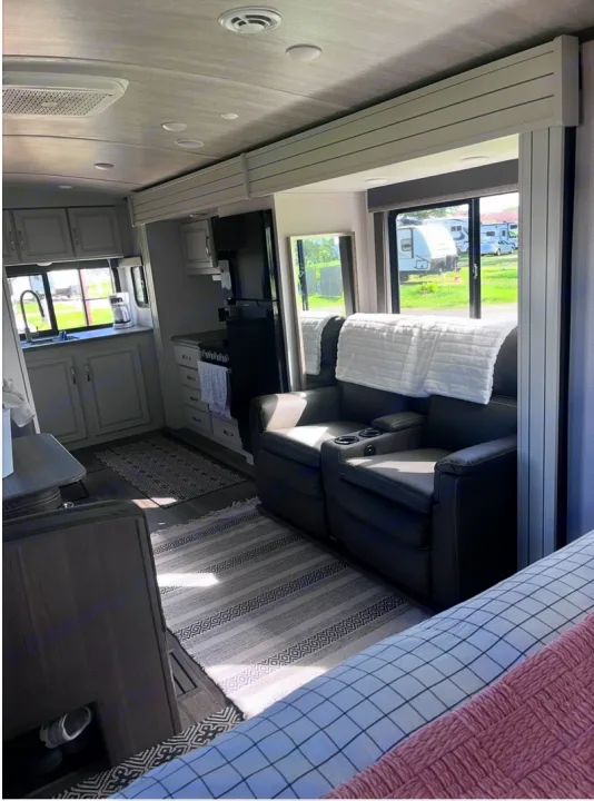 Spacious RV rental interior showcasing a modern kitchen with appliances, comfy reclining seats, and a cozy bed setup.. Keystone RV Cougar 2023