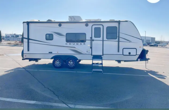 This white Cougar travel trailer, parked in a lot, is perfect for an RV rental. Ideal for camping and road trips.. Keystone RV Cougar 2023