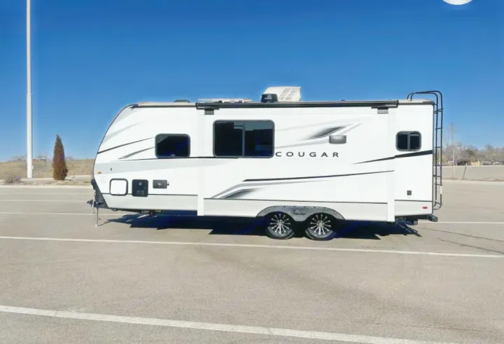 White Cougar travel trailer rv rental, a two-axle RV with dark windows, parked on asphalt under a clear blue sky.. Keystone RV Cougar 2023