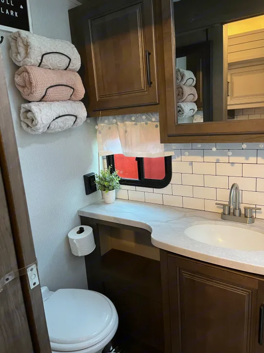 Clean RV rental bathroom featuring modern vanity, sink, toilet, and rolled towels on wall storage.. Keystone RV Cougar 2023
