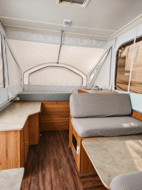 Inside a modern pop-up RV rental: light fabric walls, wood-look floor, comfortable dinette, and compact kitchen area.. Viking 1906 2001