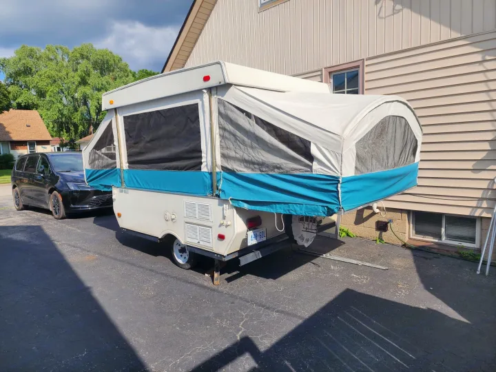 A pop-up camper, potentially an RV rental, is set up in a driveway next to a house, with a dark minivan parked in front.. Viking 1906 2001