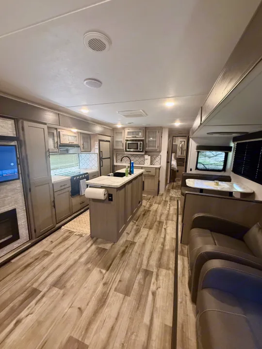 Spacious RV rental interior with a modern kitchen island, dining booth, and living area. Features light wood-look flooring.. Keystone RV 2955RL 2022