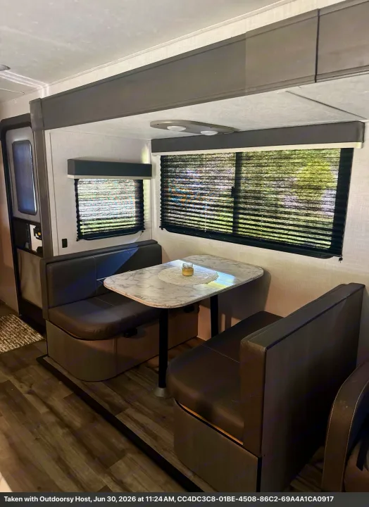 RV rental dinette with dark upholstered booth seating, a marble-patterned table, and windows with blinds drawn.. Keystone RV 2955RL 2022