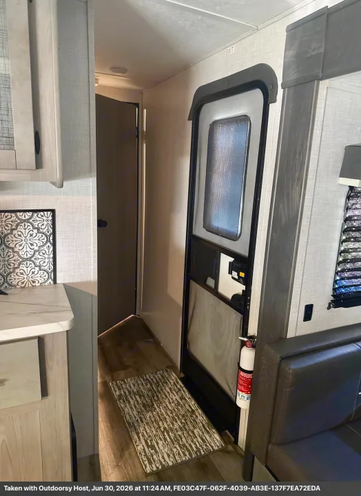 RV rental interior features main entry door, mounted fire extinguisher, and a glimpse of the kitchenette and seating area.. Keystone RV 2955RL 2022