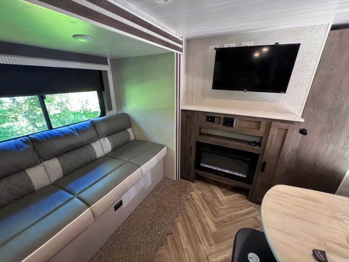 RV rental interior: Comfortable sofa by a window, entertainment unit with TV & fireplace, and dinette table in a cozy living space.. Forest River Salem Cruise Lite 2022