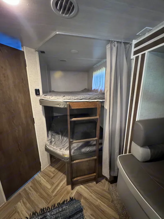 Interior of an RV rental with modern bunk beds, a ladder, gray bedding, and a sofa, creating a compact sleeping and living area.. Forest River Salem Cruise Lite 2022