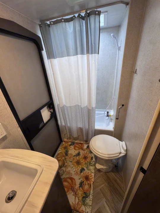 Functional RV rental bathroom with shower, toilet, sink, & a vibrant sunflower/pumpkin rug. Ideal for your journey!. Forest River Salem Cruise Lite 2022