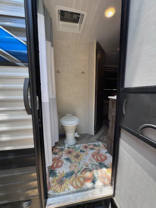Compact RV rental bathroom with a toilet, gray shower curtain, and a fall-themed mat at the entrance.. Forest River Salem Cruise Lite 2022