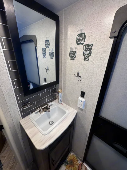 This RV rental's compact bathroom features a sink, mirror, and helpful hygiene decals on textured walls.. Forest River Salem Cruise Lite 2022