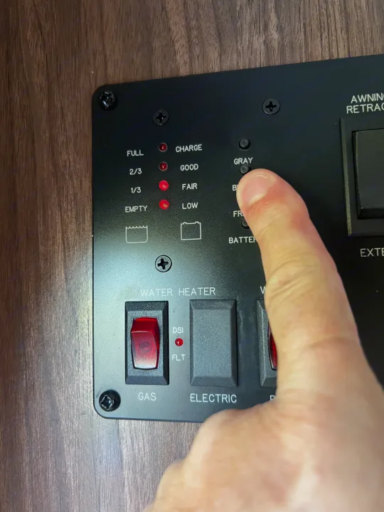 RV rental control panel. Finger presses gray tank button. Fresh water (1/3, Empty) and battery (Fair, Low) indicators lit. Gas water heater is on.. Coleman Lantern Series 2016