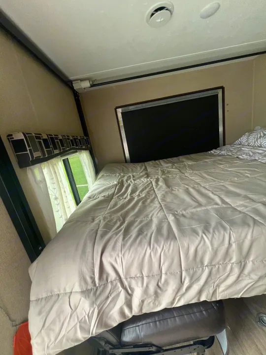 RV rental bedroom: light comforter on bed, window with curtains, and overhead vent for comfortable travel.. Coleman Lantern Series 2016
