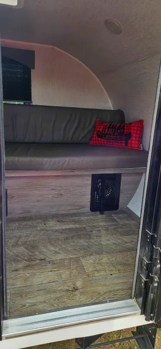 Inside this RV rental: A cozy bench seat with a red plaid pillow, wood floor, and a heater vent in the compact camper.. Sunset Park RV SunRay 2024