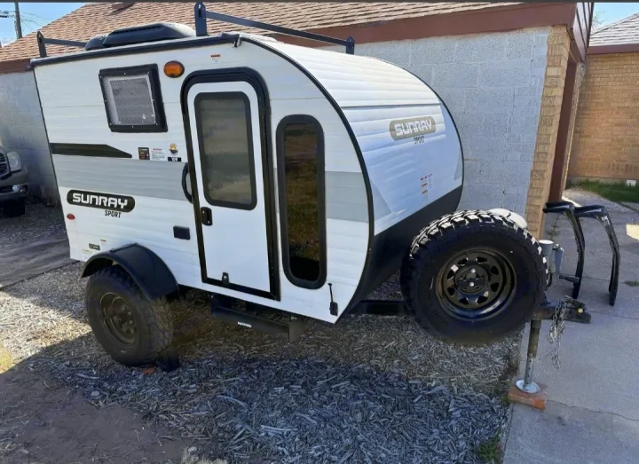 White Sunray Sport teardrop camper with off-road tires & roof rack, ideal for an RV rental adventure or camping.. Sunset Park RV SunRay 2024