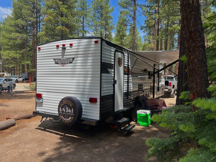 An RV rental travel trailer set up for glamping at a beautiful campground under pine trees, ready for a relaxing outdoor stay.. Forest River Wildwood X-Lite 2020