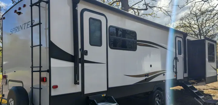 This Sprinter RV rental, a light-colored travel trailer, is ready for adventure. It features two entry doors, steps, and a rear ladder.. Keystone RV Sprinter Limited 2021