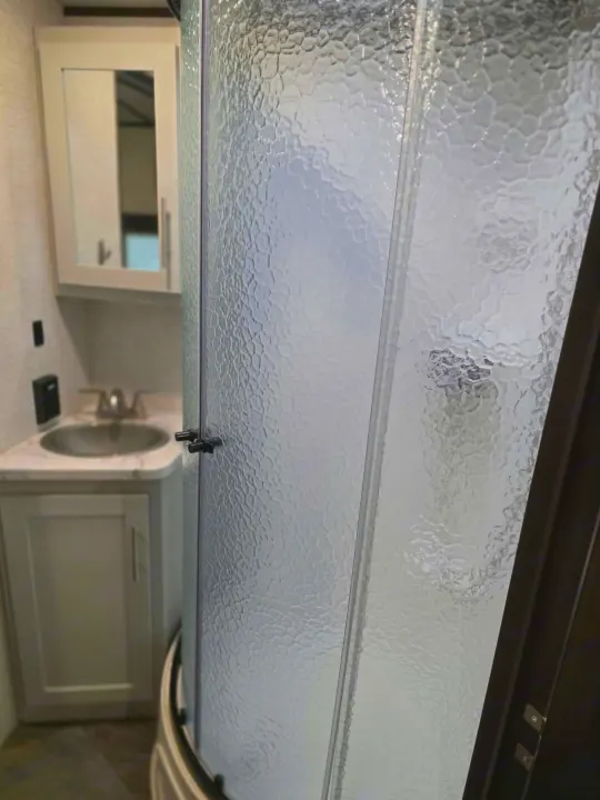 RV rental bathroom featuring a modern, textured glass shower door, a vanity with a silver sink, and a mirrored medicine cabinet.. Keystone RV Bullet Ultra Lite 2021
