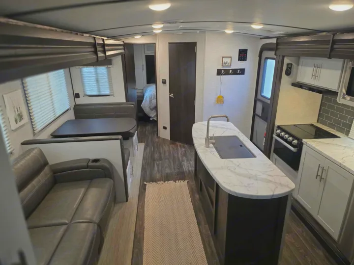 Bright RV rental with modern kitchen island, dining booth, sofa, and bedroom access, ideal for your next trip.. Keystone RV Bullet Ultra Lite 2021