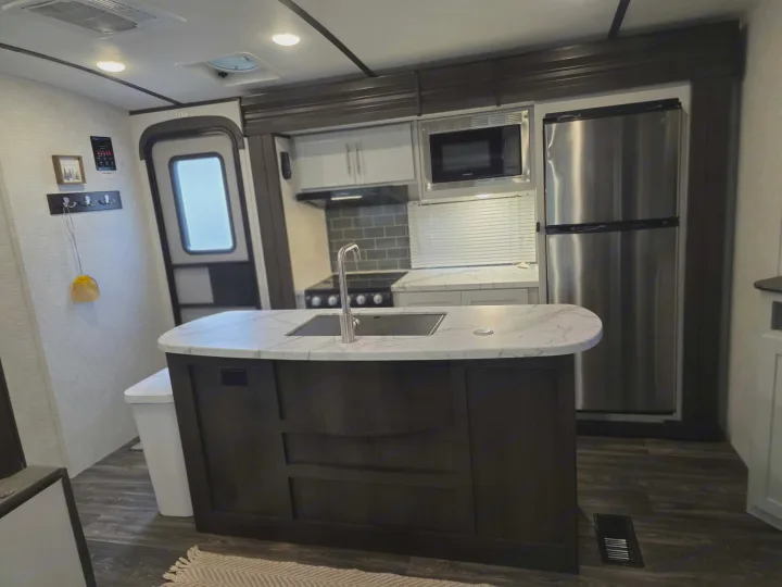 Inside this modern RV rental: a kitchen with an island, sink, stove, microwave, and stainless steel fridge.. Keystone RV Bullet Ultra Lite 2021
