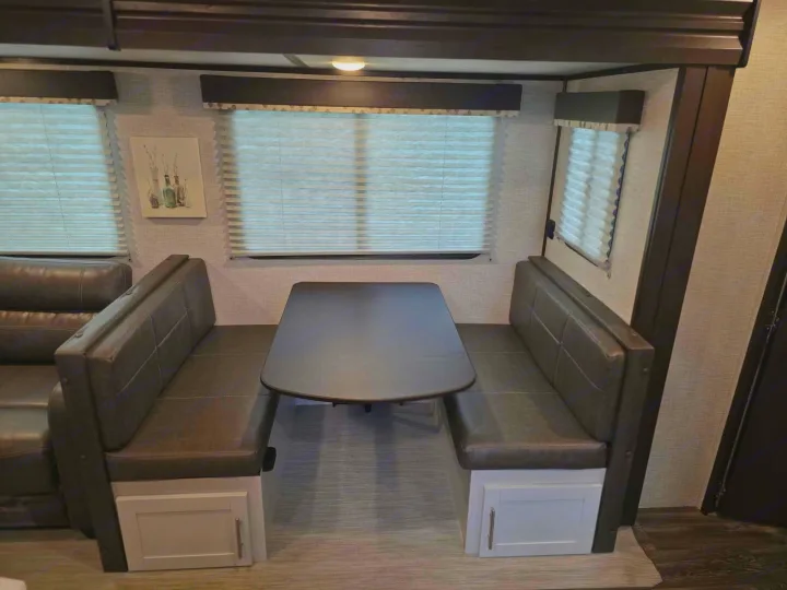 Inside this RV rental: a modern dinette booth with dark gray upholstered benches, a table, window blinds, and built-in storage.. Keystone RV Bullet Ultra Lite 2021