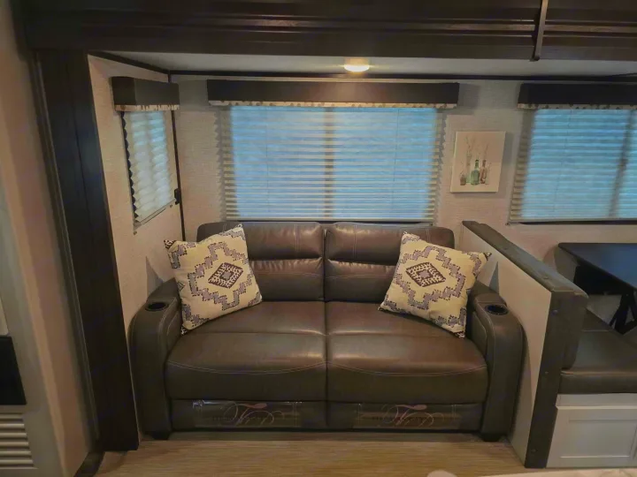 This inviting RV rental interior features a comfy gray loveseat with patterned pillows, bright windows, and a dining area.. Keystone RV Bullet Ultra Lite 2021