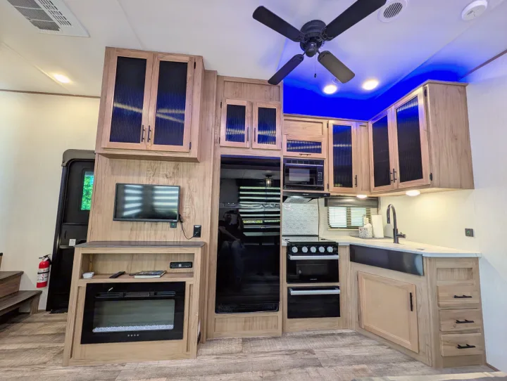Modern RV rental interior with a functional kitchen, media area (TV & fireplace), and cool blue accent lighting.. Cherokee limited Arctic Wolf 2023