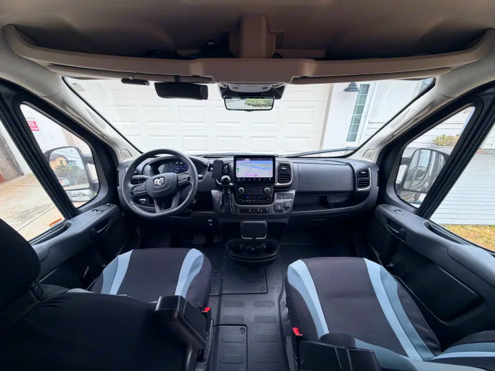 Inside an RV rental cockpit, featuring the dashboard, steering wheel, digital display, and front seats with view of a garage.. Jayco Swift 2025