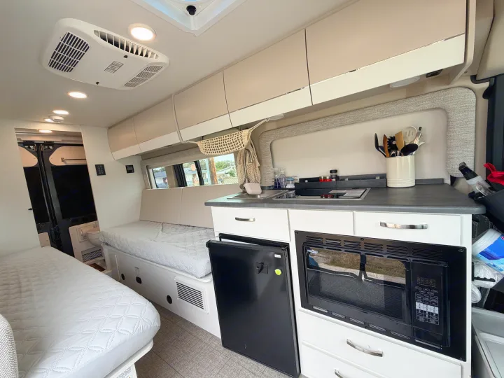 Explore this modern rv rental interior, showcasing a compact kitchen with sink, stove, microwave, fridge, and cozy sleeping areas.. Jayco Swift 2025