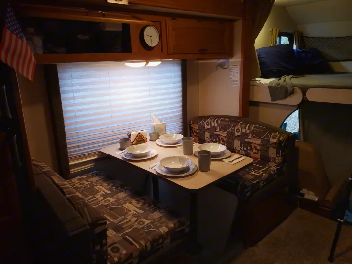 Inviting RV rental interior with a set dinette, booth seating, and a cozy bunk bed, perfect for travel.. Fleetwood Tioga 31M 2007
