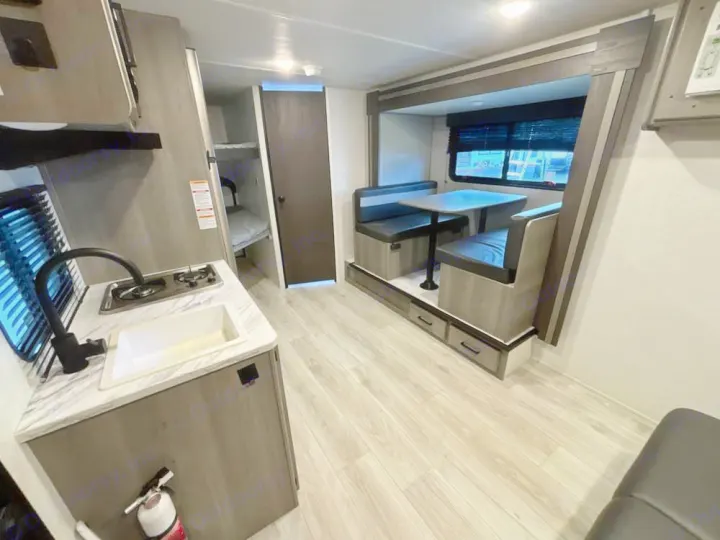 RV rental interior view: kitchenette with sink/stovetop, dining booth, and bunk beds for travelers.. Keystone RV Hideout Sport 2025