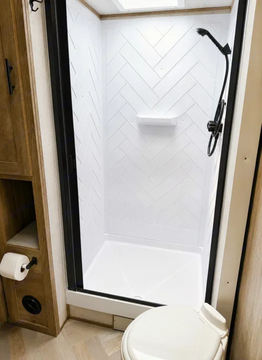 This rv rental features a bright, modern bathroom with a spacious white herringbone shower, toilet, and compact storage.. Forest River Salem 2021