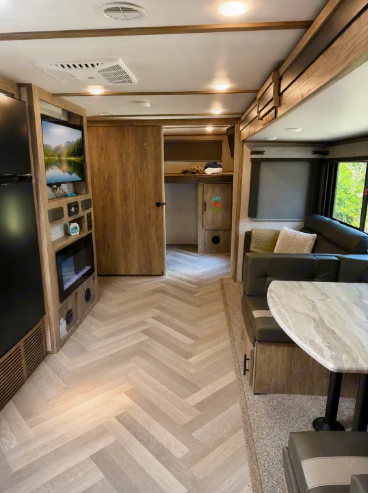 Cozy RV rental interior showcases herringbone floors, a dark sofa, dining booth, TV, and fireplace. Modern camper living space.. Forest River Salem 2021
