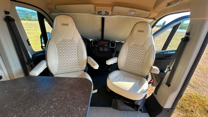 Inside an rv rental, featuring swiveling captain chairs with quilted upholstery, a dashboard, and a speckled table. Ready for adventure.. BURSTNER B66 2024