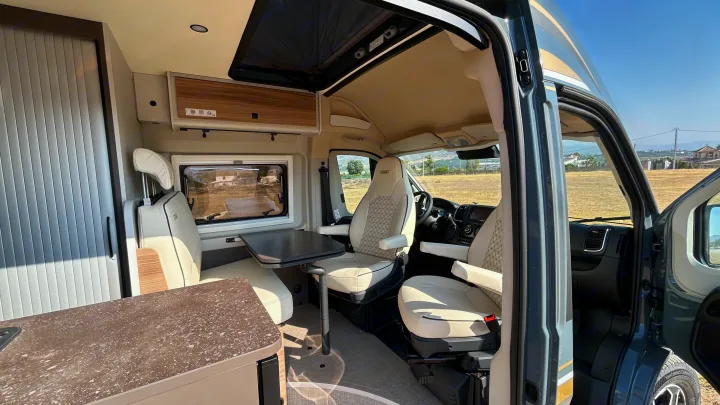 Modern rv rental camper van interior. Features a bright dining area with swivel seats, a counter, and overhead storage.. BURSTNER B66 2024