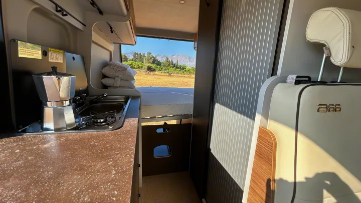Inside an rv rental: a compact kitchen with a moka pot, cozy bed, and an expansive mountain landscape view.. BURSTNER B66 2024