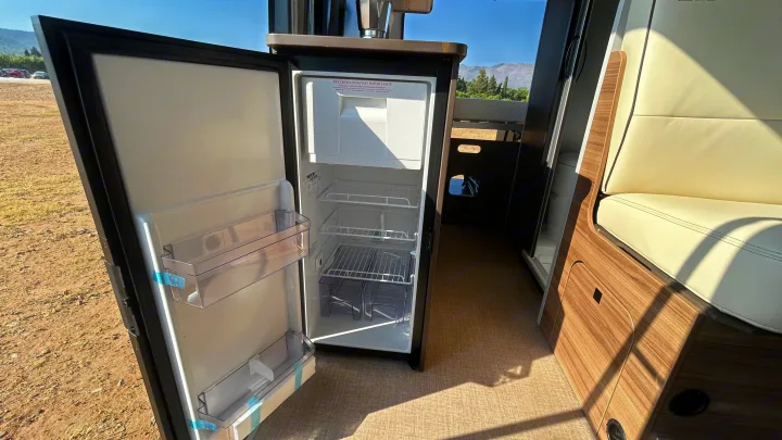 An RV rental's open refrigerator shows shelves and door storage, with plush seating and sleek wooden cabinetry in the interior.. BURSTNER B66 2024