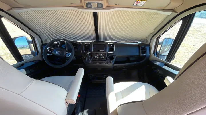 Bright interior of an RV rental with sunshade deployed, comfy white seats, and a Fiat dashboard. Ready for travel!. BURSTNER B66 2024
