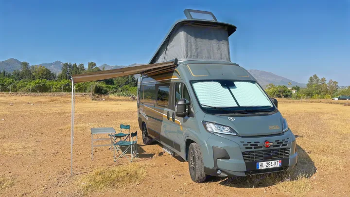 RV rental: A gray camper van with an extended pop-top, awning, table, and chairs in a sunny, dry mountain setting.. BURSTNER B66 2024