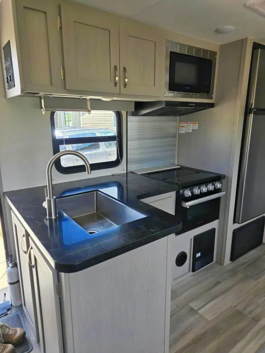 Spacious rv rental kitchen: light wood cabinets, dark counters, stainless sink, stovetop/oven, microwave, and refrigerator.. Forest River Tracer 2022