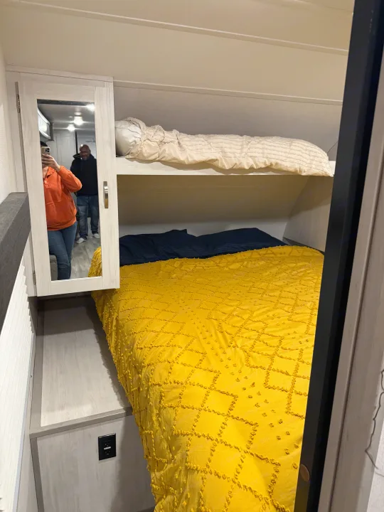 Cozy RV rental bedroom with bright yellow bunk beds and mirrored cabinet. Compact sleeping space ideal for travel.. Forest River Tracer 2022