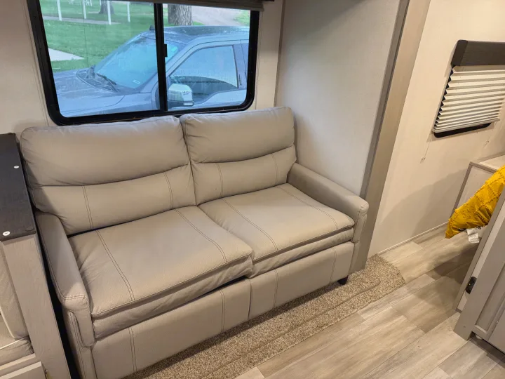 Cozy light gray sofa in an RV rental, with a window view showing a truck and outdoor scenery from inside the trailer.. Forest River Tracer 2022