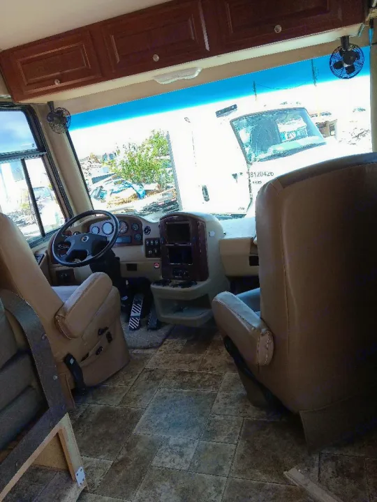 Spacious RV rental cockpit with beige seats, steering wheel, and patterned floor tiles. Road view ahead through the windshield.. Thor Palazzo 2014