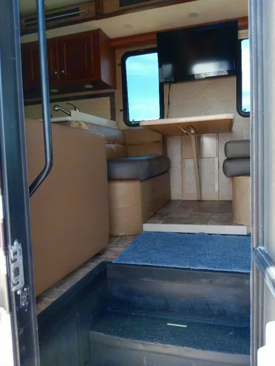 Interior view of an RV rental: dining area with table, TV, kitchen counter, and entry steps. Ready for your trip.. Thor Palazzo 2014
