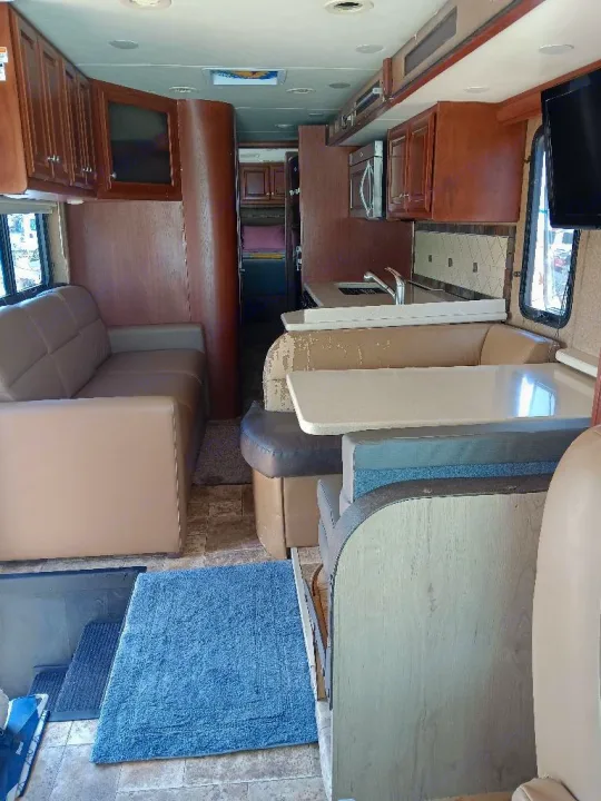 Spacious RV rental interior featuring a living area with a couch, a kitchen, and a dinette, all with warm wood tones.. Thor Palazzo 2014