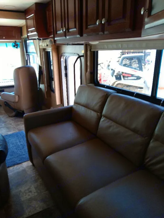 Experience comfort in this **rv rental's** living area, featuring a brown sofa, wood cabinets, and front captain's chair.. Thor Palazzo 2014